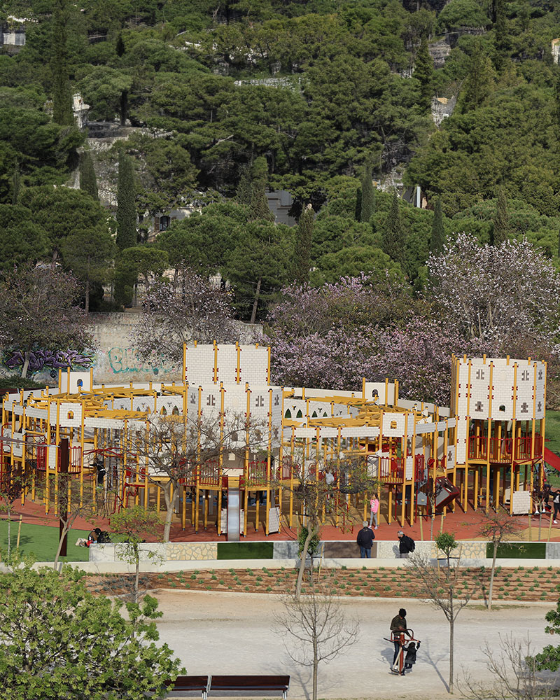 A very large playground unit, which is castle themed, it is very big nestled amongst a huge park with urban spaces around it.